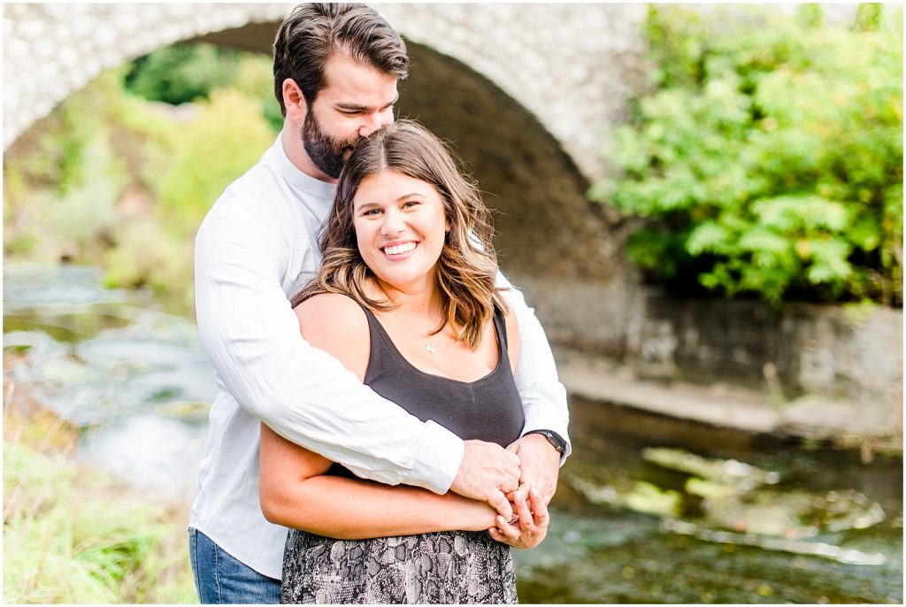 Spencer Gorge Engagement Session couple snuggling in front of bridge by water