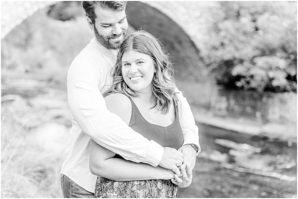 Spencer Gorge Engagement Session couple snuggling in front of bridge by water