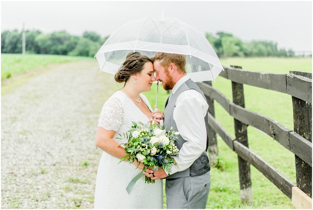 Princeton backyard wedding bride and groom nuzzling under a clear umbrella in the rain