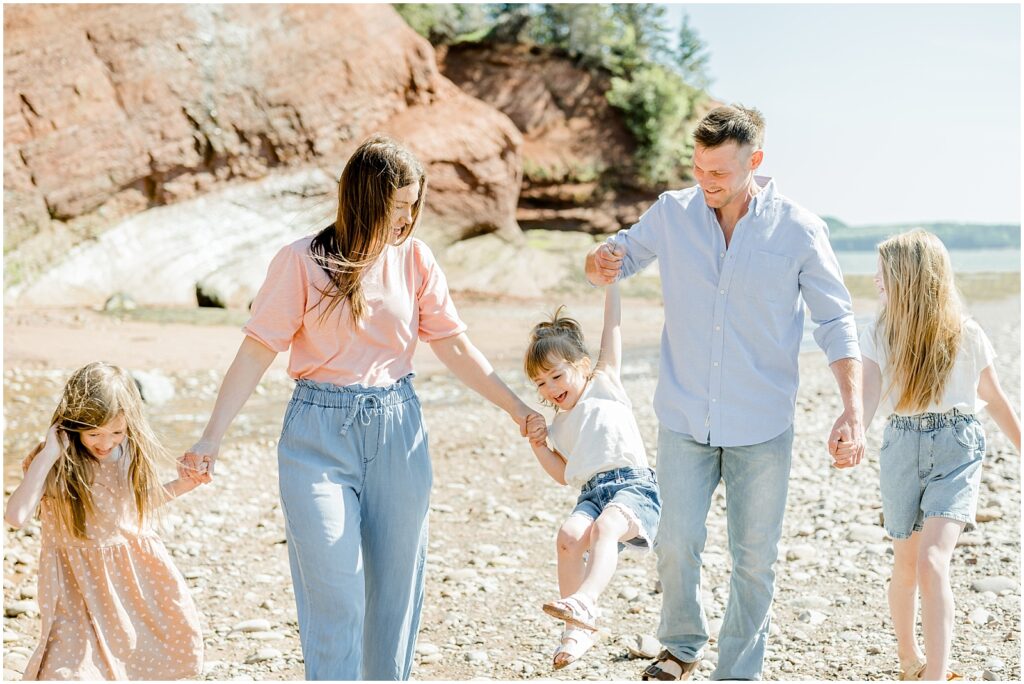 family holding hands swinging toddler in the air on the shore 