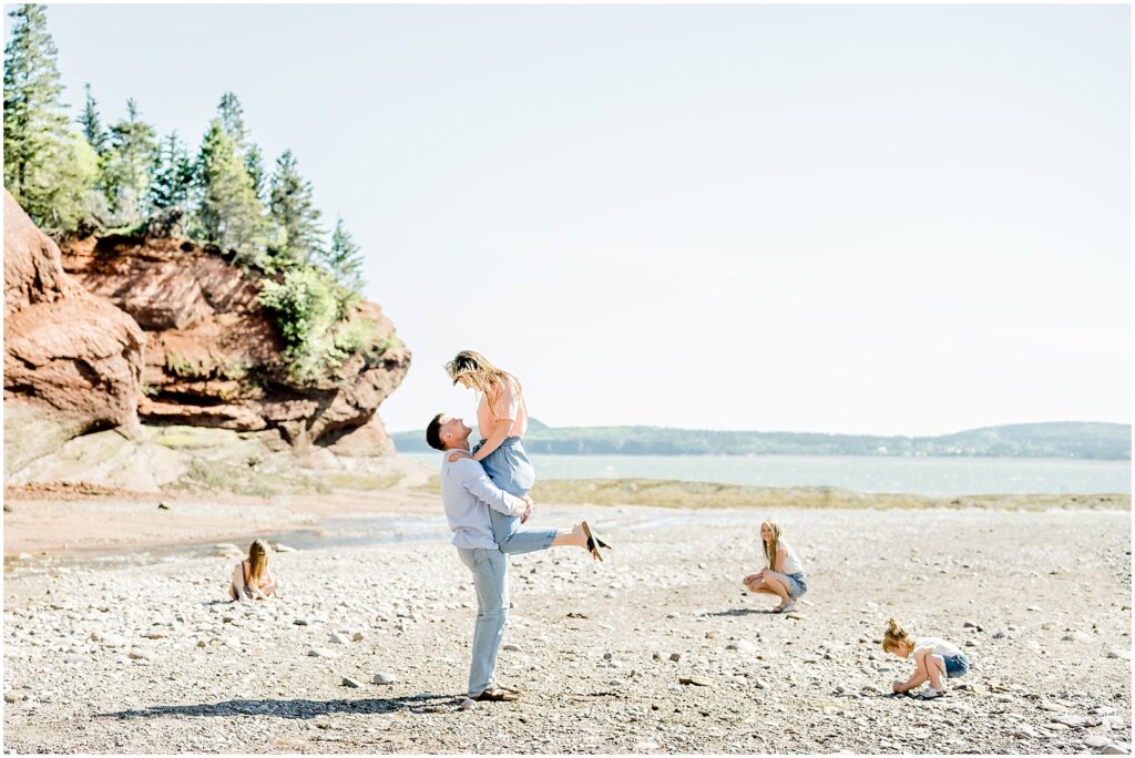 Saint Martins Portrait Session husband picking up wife and gazing into her eyes while the kids play on the shore