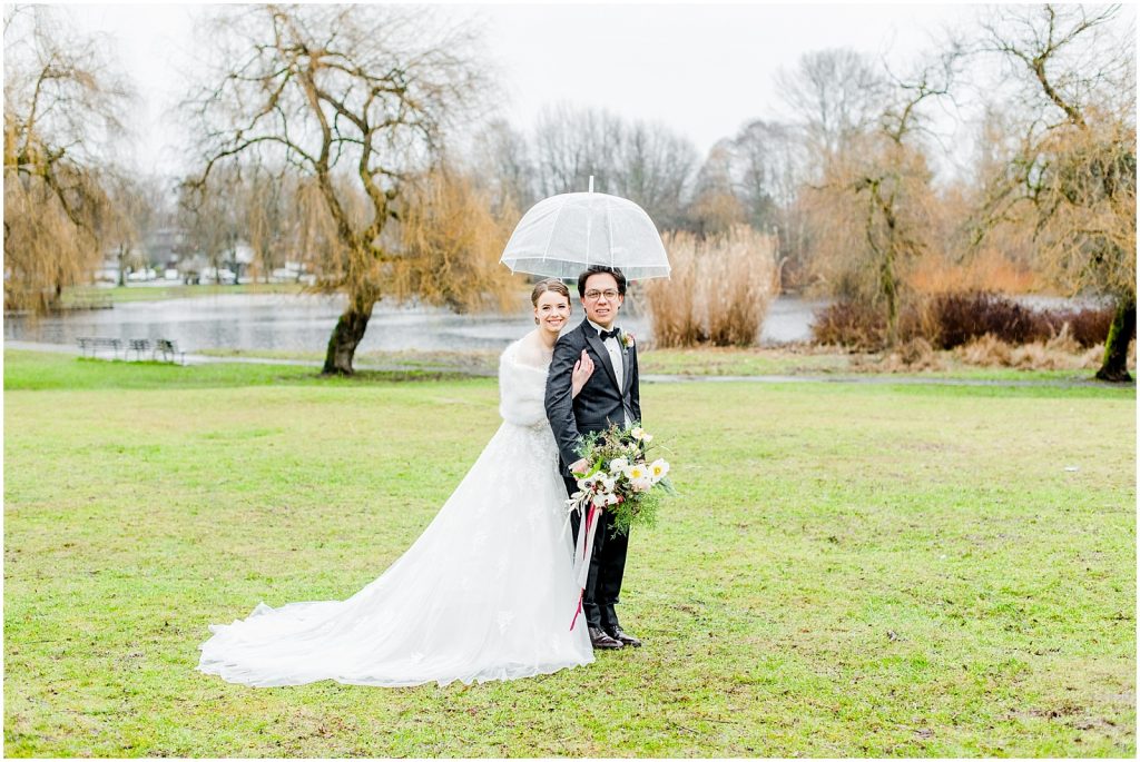 burnaby vancouver wedding bride hugging groom at Trout Lake under umbrella